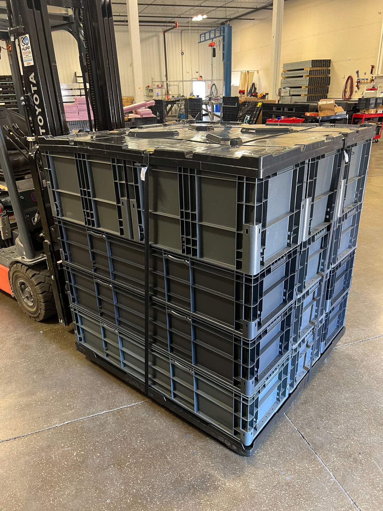 Straight wall totes stacked on plastic pallet with seat belt fastening pallet to top cap lid